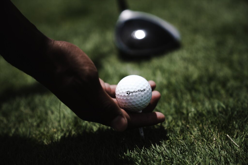 Person Holding White Golf Ball on Ground