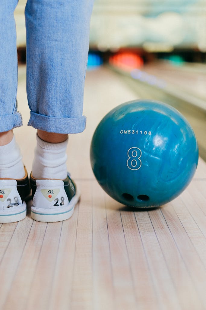 Close-up of a woman ready to bowl, featuring legs and a bowling ball in a lane.