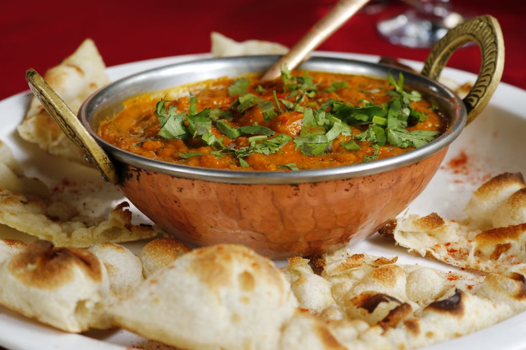 Delicious Indian curry garnished with cilantro served with naan in a copper dish.