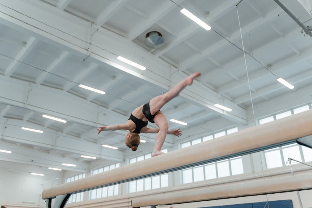 Female gymnast performing an impressive move on the balance beam indoors.