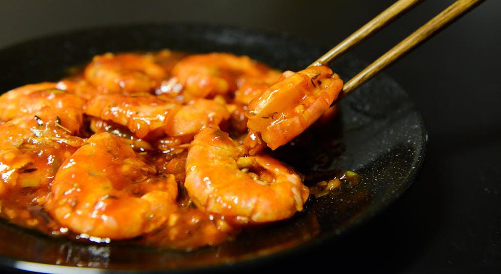 Close-up of spicy prawns in sauce with chopsticks on a dark plate